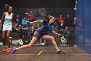 AJN Steelstock sponsored Emma Bartley lunging to hit a squash ball with an audience watching