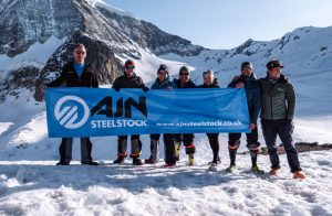 Mountain climbers holding AJN banner at the top of a snowy mountain